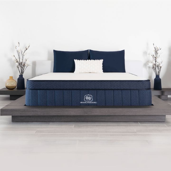 Blue mattress with white bedding on a wooden bed frame in a bedroom setting.